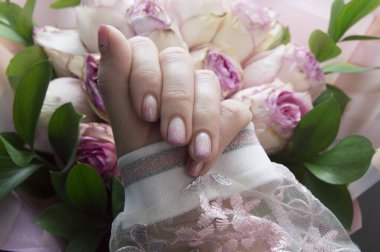 Tırnaklarında pembe manikür ve güller olan bir kadının eli.