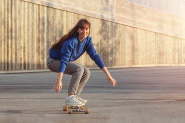 Şehir merkezinde kaykay süren bir kadın. Kadın kaykaycı mavi kazak giyer..