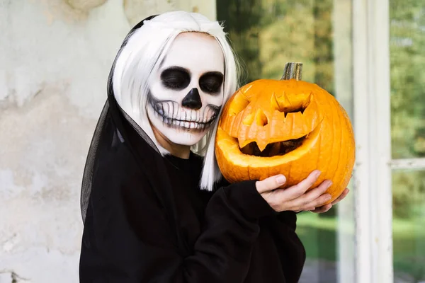 Retrato de mujer en vestido negro con maquillaje de cráneo con calabaza tallada. —  Fotos de Stock