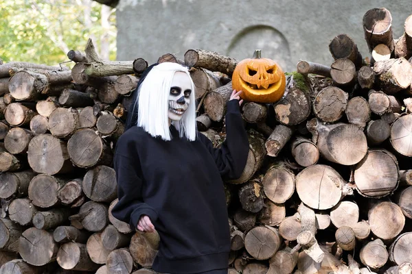 Retrato de la novia muerta, que está de pie cerca de los troncos aserrados. Junto a la calabaza tallada para Halloween —  Fotos de Stock