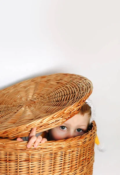 Kleine Niedliche Junge Porträt Sitzt Und Versteckt Weidenkorb Unter Mütze Stockbild