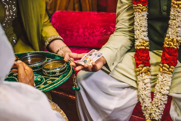 ドバイ アラブ首長国連邦のインドパキスタン人専門家の手サンゲットの結婚式の夜の儀式の間に 手にお金の汚れと女性と新郎 金色のヘナとMendiベルベットプレート ストック画像
