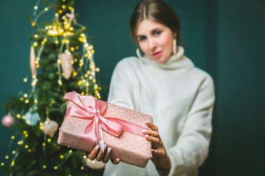Güzel pembe Noel 'e ve yeni yıl hediye kutusuna odaklan. Süslü ağaçlı kadın ellerinde kurdele olsun.