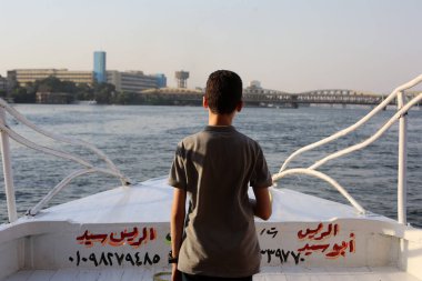 Kahire, Mısır - 08.13.2017: Genç çocuk teknede kalır ve Nil nehri suyu, binalar ve köprüsü olan güzel şehir manzarasına bakar