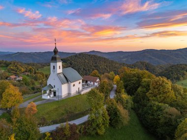 Günbatımında Dolsko pri Ljubljani 'nin tepesindeki Kutsal Haç Kilisesi (Sveti Kri) ve Krievska vadisinin yemyeşil ve dalgalı tepelerle çevrili çarpıcı hava manzarası..
