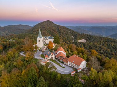 Meryem 'in Doğuşu Kilisesi' nin ve günbatımında Zasavje 'nin 852 metre yüksekliğindeki kutsal dağının tepesindeki savunma duvarının hava manzarası, sonbahar ormanlarıyla çevrili..