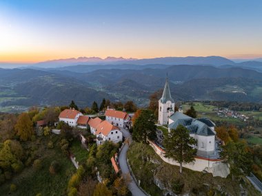 Meryem 'in Doğuşu Kilisesi' nin ve günbatımında Zasavje 'nin 852 metre yüksekliğindeki kutsal dağının tepesindeki savunma duvarının hava manzarası, sonbahar ormanlarıyla çevrili..