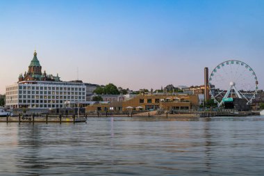 Helsinki Katedrali 'nin yeşil kubbeleri, diğer şehir binaları ve sakin su üzerinde SkyWheel Helsinki' nin yer aldığı, Helsinki rıhtımının alacakaranlıktaki panoramik manzarası.