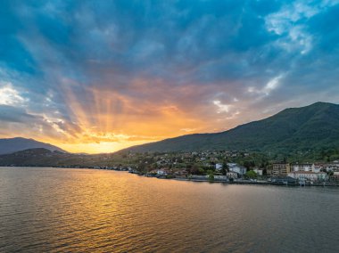 Güneş doğarken Maggiore Gölü 'ndeki Porto Valtravaglia kıyı kasabasının havadan görünüşü limanı, renkli binaları ve kasabanın arkasındaki sarp orman tepelerini gösteriyor.