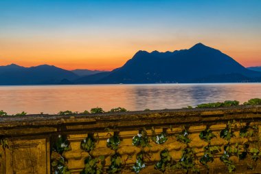Wide panoramic view of Lake Maggiore and the surrounding Alps, with the silhouette of Monte Mottarone visible across the water, captured during the blue hour of dawn
