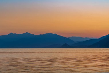 Maggiore Gölü 'nün panoramik manzarası ve Alpler ve dağların silueti (muhtemelen Mottarone), Stresa' dan gelen parlak turuncu ve mavi renkleri yansıtır.