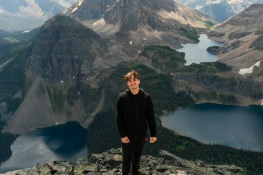 Hiker poses triumphantly amidst towering mountains and serene alpine lakes.
