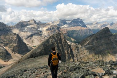 Mountain Hiker: Backpacker overlooking a vast mountain range under cloudy sky.