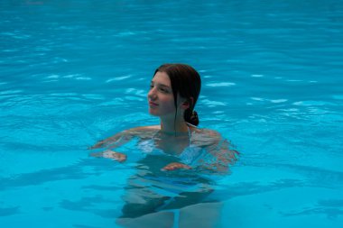 Parlak turkuaz renkli bir yüzme havuzunda rahatlatıcı bir yüzüşten zevk alan bir kadın. Radyum Kaplıcaları, BC