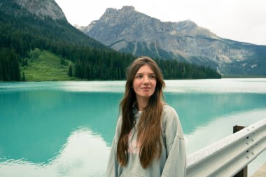 Genç bir kadın, el değmemiş bir gölün ve engebeli dağların arkasında. Zümrüt Gölü, BC