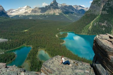 Kadın, el değmemiş sulara bakan bir kaya çıkıntısında huzurlu bir anın tadını çıkarıyor. OHara Gölü, BC