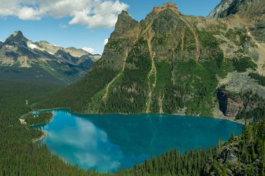 Canlı mavi bir göl manzarası bulutlu gökyüzünü ve dağı yansıtıyor. OHara Gölü, BC
