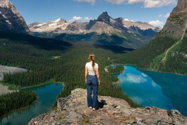 Kadın bir uçurumdan dağların, ormanın ve gölün manzarasını düşünüyor. OHara Gölü, BC