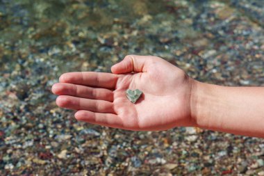 Temiz ve sığ suların üzerinde kalp şeklinde bir taşı tutan bir el. Waterton, AB