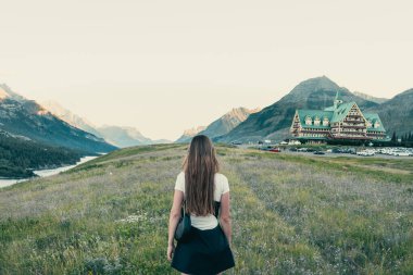 Bir tarlada durmuş, dağlara ve manzaralı bir otele bakan bir kadın. Waterton, AB