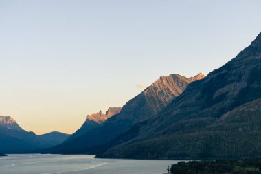 Huzurlu bir göl ve yüksek tepeler içeren manzaralı dağ manzarası. Waterton, AB
