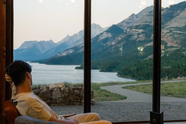Adam pencereden dağ manzarası seyretmeyi düşünüyor. Waterton, AB