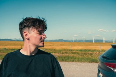 Düşünceli bir adam açık bir yolculukta yel değirmenlerini gözlemler, yukarıdaki mavi gökyüzünü. Pincher Creek, AB