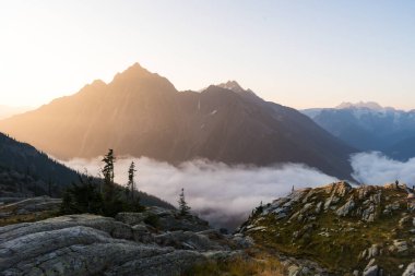 Gün boyunca puslu bulutların tersine döndüğü panoramik dağ manzarası. Buzul Ulusal Parkı, BC