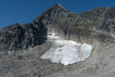 Parlak güneşli bir günde mavi gökyüzünün altında buzlu karla kaplı bir dağ. Buzul Ulusal Parkı, BC