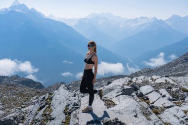 Atletik kadın bir dağın tepesinde poz veriyor, manzaranın tadını çıkarıyor. Buzul Ulusal Parkı, BC