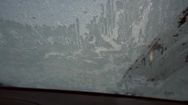 Donmuş bir arabanın ön camı temiz, kış sabahı rutini, ev işleri. Adam donmuş buzu kazıyor, arabadan kar yağıyor - 4K Stock Video