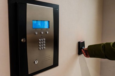 Bu görüntü, bir binaya girmek için anahtar kullanan birini gösteriyor. Klavye ve kart okuyuculu bir güvenlik sistemi duvara monte edilmiş, kimin girebileceğini kontrol ediyor.
