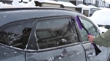 Bir arabanın camından kar ve buz kazıyan bir elin yakından görüntüsü. Yansıma olarak görünen adamla birlikte..