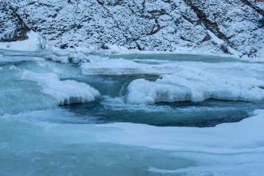 Akıntı, buz oluşumları ve karla kaplı kayalarla kısmen donmuş bir nehirden oluşan çarpıcı bir kış manzarası. Soğuk, doğa ya da macera taşımak için ideal.