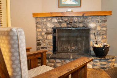 Rahat bir odada döşeme koltuğunun yanında yakacak odunlu taş bir şömine var. Sıcak tonlar ev ortamında rahatlatıcı ve davetkar bir atmosfer yaratır.