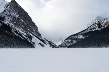 Bulutlu bir gökyüzünün altındaki karla kaplı dağlar arasında sakin bir vadi. Sakinleştirici bir kış manzarası, seyahat, macera ve doğa temalı projeler için mükemmel.