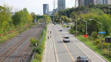 Toronto, ON, Kanada - 30 Ekim 2025: Tren raylarına bitişik bir yolda arabaların ve bisikletçilerin dinamik hareketlerini gösteren bir hava görüntüsü