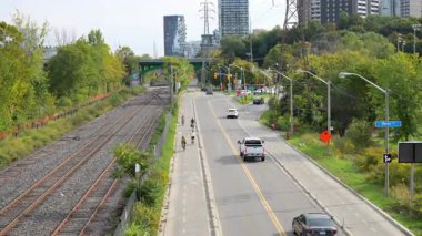 Toronto, ON, Kanada - 30 Ekim 2025: Aktif tren raylarının yanındaki bir şehir yolunda gidip gelen araba ve bisikletçilerin yavaş çekim görüntüsü