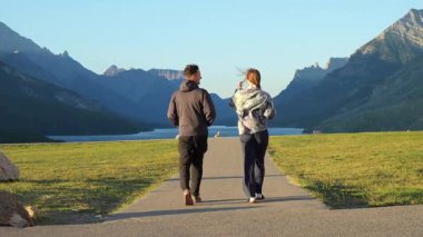 Bir çift dağ gölü ve yeşil çimlerle manzaralı bir patika boyunca yürüyor, dışarıda huzuru hissediyorlar. Waterton, AB, Kanada