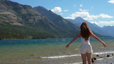 Mutlu kadın güzel dağ zirveleri ve açık mavi gökyüzü olan bir göl kıyısına uzanır. Waterton, AB, Kanada