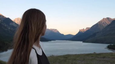 Gün batımında dağ manzarasının keyfini çıkaran mutlu genç bir kadının yakın çekimi. Seyahat içeriği için ideal. Waterton, AB, Kanada
