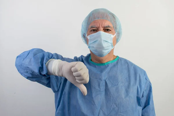 The main subject is out of focus, old senior male surgeon stand white background uniform doctor health care emergency profession help people thumbs down hand symbol medical gloves surgical hair net