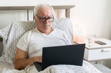 Yaşlanan son sınıf öğrencisi, yataktaki dairede çalışıyor. Emekliler için dizüstü bilgisayar işleri yapıyor.