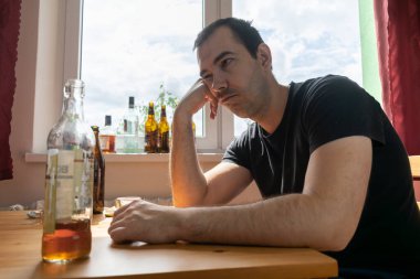 Genç erkek adam evde yalnız başına alkol şişesi içiyor üzgün alkolizm belirtileri ve semptomlar rehabilitasyon ve iyileşme sorunları yaşıyor.