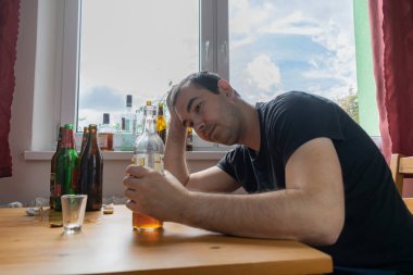 Genç erkek adam evde yalnız başına alkol şişesi içiyor üzgün alkolizm belirtileri ve semptomlar rehabilitasyon ve iyileşme sorunları yaşıyor.