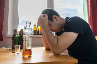 Genç erkek adam evde yalnız başına alkol şişesi içiyor üzgün alkolizm belirtileri ve semptomlar rehabilitasyon ve iyileşme sorunları yaşıyor.