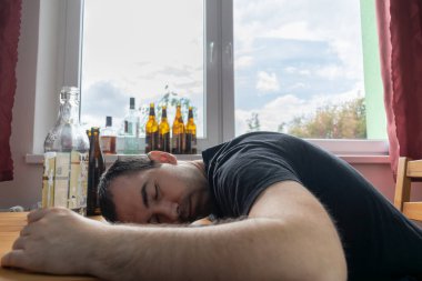 Genç erkek adam evde yalnız başına alkol şişesi içiyor üzgün alkolizm belirtileri ve semptomlar rehabilitasyon ve iyileşme sorunları yaşıyor.