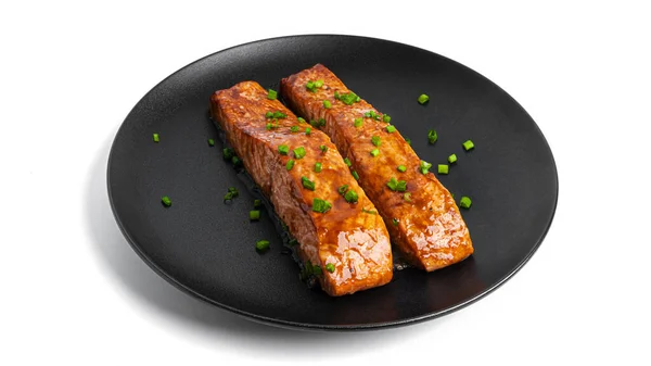 Salmon panggang dengan kecap dengan herbal di piring hitam terisolasi pada latar belakang putih. Stok Gambar