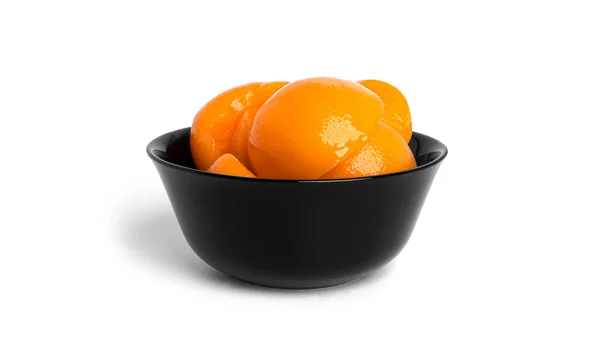 Persikor på burk i en svart skål. Söta persikor i sirap isolerad på vit bakgrund. — Stockfoto