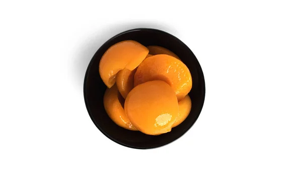 罐装桃子放在一个黑色碗里.白底糖蜜中的甜桃子. — 图库照片